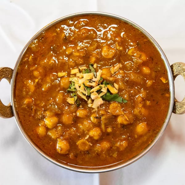 A close-up of a bowl of Masala Indian Cuisine's Chana Masala, garnished with ginger and cilantro.