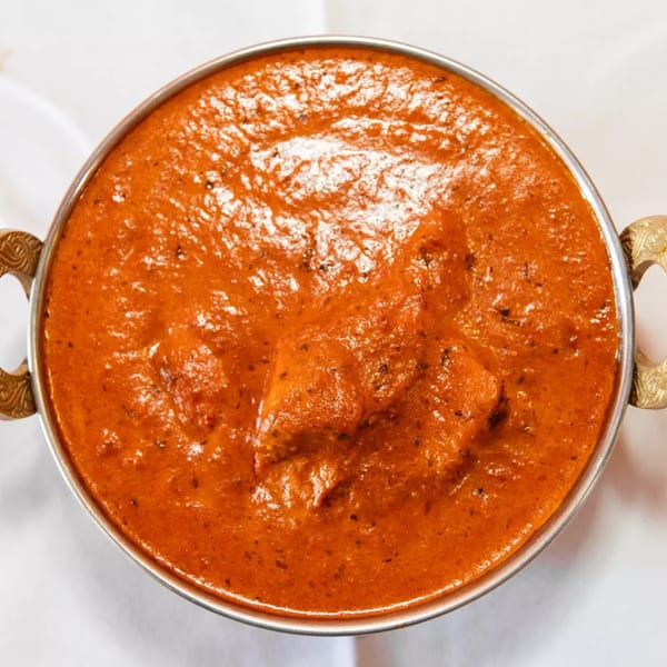 Masala Indian Cuisine's butter chicken, a rich orange curry with chicken pieces, served in a metal bowl.